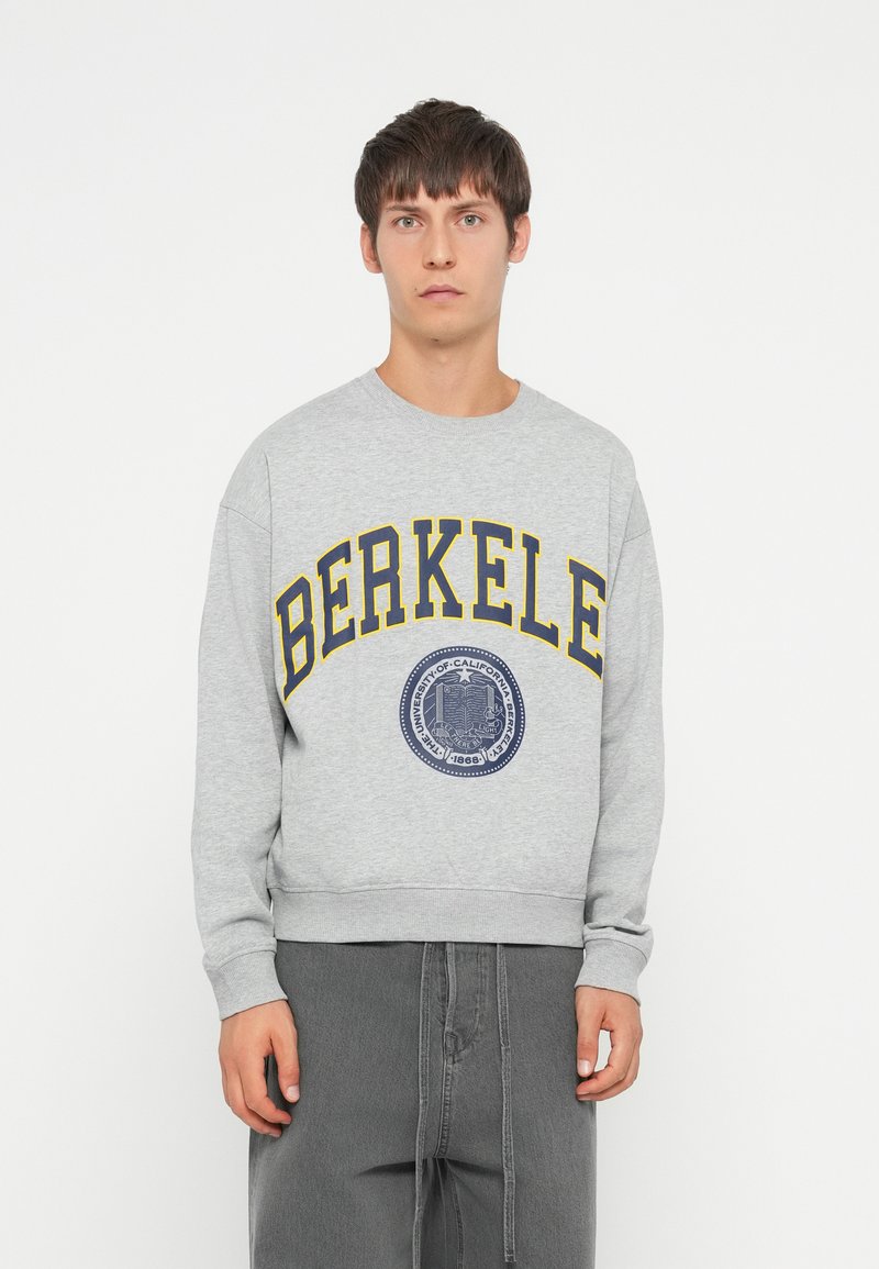Gray sweatshirt with yellow letters spelling "BERKELE" and a navy emblem. Features ribbed cuffs and waistband, with a relaxed fit.