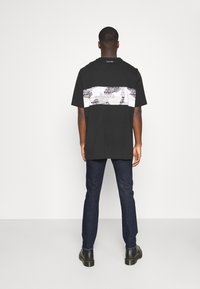 Czarna koszulka z krótkim rękawem z białym poziomym paskiem z powtarzającym się logo "Calvin Klein". Do tego ciemne dżinsy.