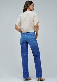 Jeans in denim blu con taglio dritto, dotati di tasche posteriori e una finitura sbiadita. Abbinati a un top beige chiaro, corto con maniche corte.
