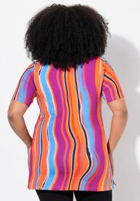 Túnica de manga corta de vibrantes rayas en naranja, púrpura, azul y negro; hecha de una tela suave con un corte holgado y aberturas en los laterales.