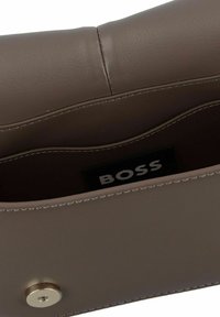 Borsa a tracolla in pelle marrone con una superficie liscia, dotata di una tasca interna e una chiusura a scatto. Include un'etichetta con la scritta "BOSS" visibile.
