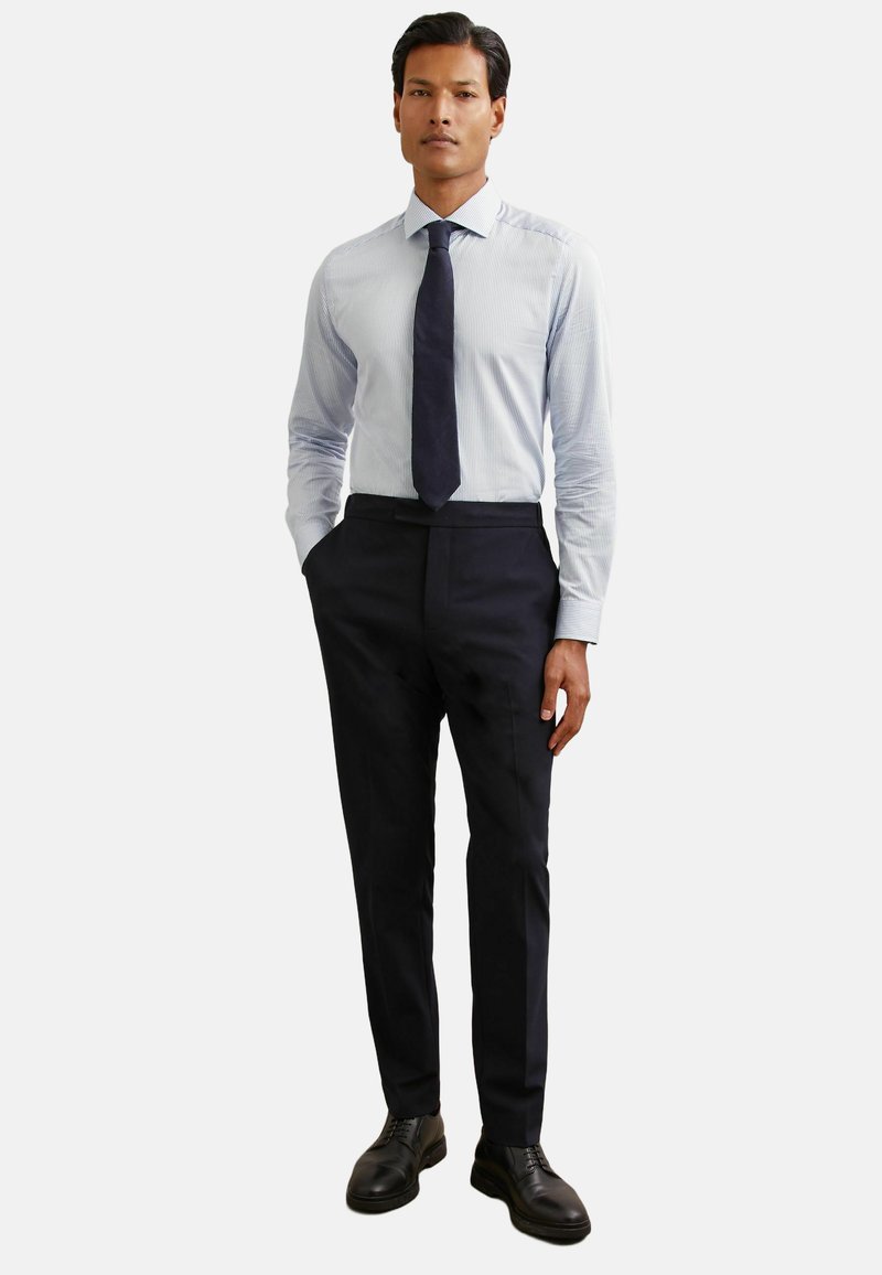 Pánsky formálny outfit: svetlomodrá pásikavá košeľa, tmavé upravené nohavice a čierne topánky. Košeľa má dlhé rukávy a štandardný golier.