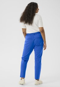 Modré kalhoty s elastickým pasem, slim fit, s zadními kapsami a hladkým povrchem. Nosené s bílým vrškem a světlými botami.
