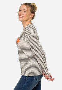 Randig långärmad skjorta i beige och marinblå, med en orange stjärnaccent på bröstet och en avslappnad passform med uppvikta ärmar.