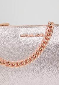 Gros plan sur un sac Michael Kors argenté métallisé texturé avec une fermeture éclair en or rose et une bandoulière chaîne liée.