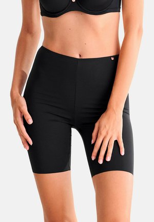 Femme portant un short de cyclisme noir taille haute ajusté et un soutien-gorge noir, debout les mains détendues le long du corps.