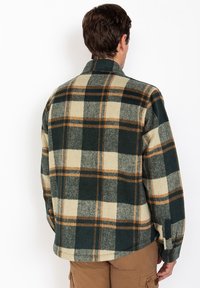 Camicia a scacchi in flanella verde, crema e arancione con colletto e polsini abbottonati. Tessuto morbido, vestibilità ampia e dettaglio dell'orlo curvo.