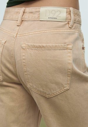 Lichtbeige denim jeans met een hoge taille, met achterzakken en een merklabel op de tailleband. Subtiele stikseldetails zichtbaar.
