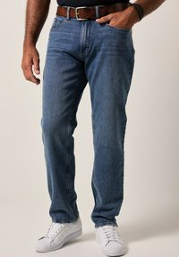 Jeans de mezclilla azul con un diseño de pierna recta, estilo de cinco bolsillos y un desvanecimiento sutil. Llevados con un cinturón de cuero marrón y zapatillas blancas.