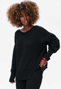 Pull noir en maille avec une coupe ample, ourlet côtelé et manches longues. Des fentes sur les côtés et des détails de tissu texturé ajoutent un intérêt visuel.