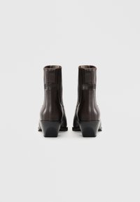 Botine din piele maro, cu un finisaj neted, toc mic și detalii fine de cusătură de-a lungul cusăturilor. Vederea din spate evidențiază un design simplu.