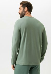 Chemise à manches longues en coton vert clair à la texture lisse, col rond et coupe décontractée, associée à un pantalon assorti.