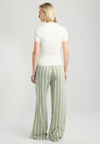 White ribbed short-sleeve top paired with wide-leg striped pants in green, blue, and yellow. Smooth texture, relaxed fit, and vertical stripes.