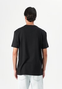 Black short-sleeve t-shirt made of cotton, featuring a crew neck and a relaxed fit, worn with light blue denim jeans.