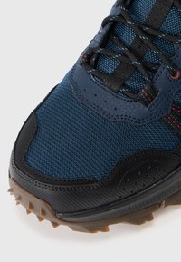Buty sportowe z teksturowaną niebieską siateczką, czarnymi syntetycznymi nakładkami oraz wytrzymałą gumową podeszwą z wyraźnymi wypustkami zapewniającymi dobrą przyczepność.