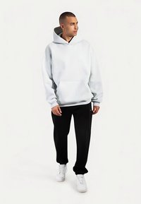 Felpa con cappuccio grigio chiaro con tasca frontale e coulisse sul cappuccio. Abbinata a pantaloni neri e sneaker bianche. Vestibilità comoda.