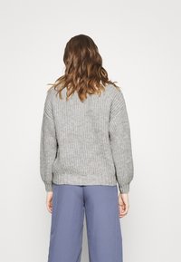 Pull en maille gris à coupe ample, avec des poignets et un ourlet côtelés, associé à un pantalon large bleu clair, vu de dos. Texture lisse.