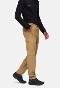 Spodnie cargo w kolorze beżowym, o luźnym kroju, z kieszeniami bocznymi, elastycznym pasem i gładką, trwałą fakturą. Połączone z czarnymi butami.