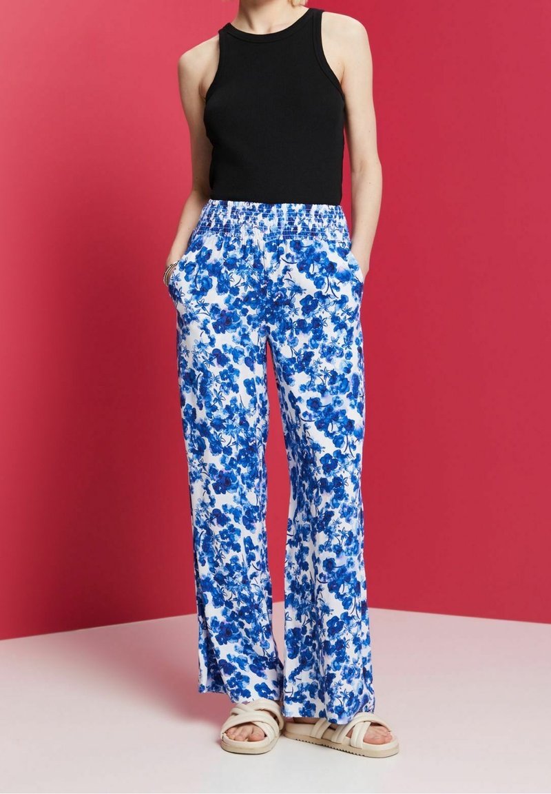 Svart ärmlös topp, blommiga blå och vita vida byxor med elastisk midja och sidofickor, kombinerat med ljusbeige sandaler.
