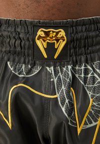 Black shorts with a textured, elastic waistband featuring a gold snake logo. Design includes gray snake patterns and yellow accents.