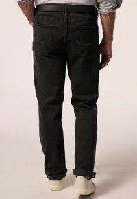 Vaqueros de denim negro con un corte recto, que cuentan con dos bolsillos traseros y un dobladillo visible. Llevados con un cinturón de cuero negro y zapatillas blancas.