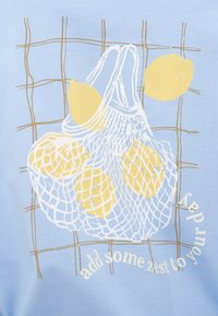 Ανοιχτό μπλε μπλουζάκι με λευκό και κίτρινο σχέδιο ενός διχτυού με λεμόνια. Το κείμενο λέει "πρόσθεσε μια φρεσκάδα στη μέρα σου" με λευκά γράμματα.