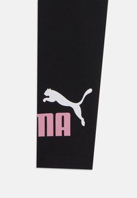 Leggings noirs avec un logo Puma blanc et un texte rose. Matière douce avec une texture lisse. Le logo représente un design de chat en train de sauter.