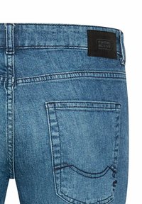 Blauwe denim jeans met een zwart label met de tekst "Camel Active," voorzien van twee achterzakken en zichtbare stiksels.