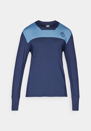 Haut de sport à manches longues en tissu évacuant l'humidité ; corps bleu foncé avec des accents bleu clair aux épaules et un petit logo sur la poitrine.
