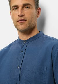 Blaues Baumwollhemd mit Stehkragen, ausgestattet mit einer vorderen Knopfleiste, zwei Knöpfen und einer Brusttasche. Glatte Textur und lässiges Design.