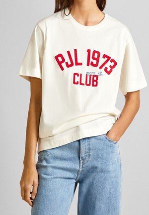 Cremefarvet bomulds-t-shirt med rød vintage-agtig tryk "PJL 1973 KLUB FYS. UDD." og korte ærmer, parret med lyseblå denim jeans.