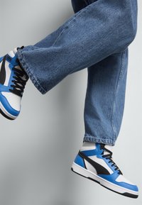 Blauwe en witte hoge sneakers met zwarte accenten. Glad leren en textielmateriaal. Geperforeerd teengedeelte en contrasterende zool.