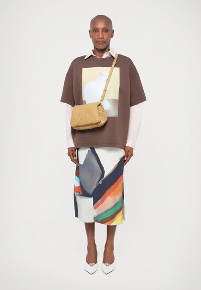 Sweatshirt oversized castanho com uma impressão gráfica, sobre uma camisa rosa clara. Saia com padrão abstrato colorido. Bolsa transversal texturizada amarela.
