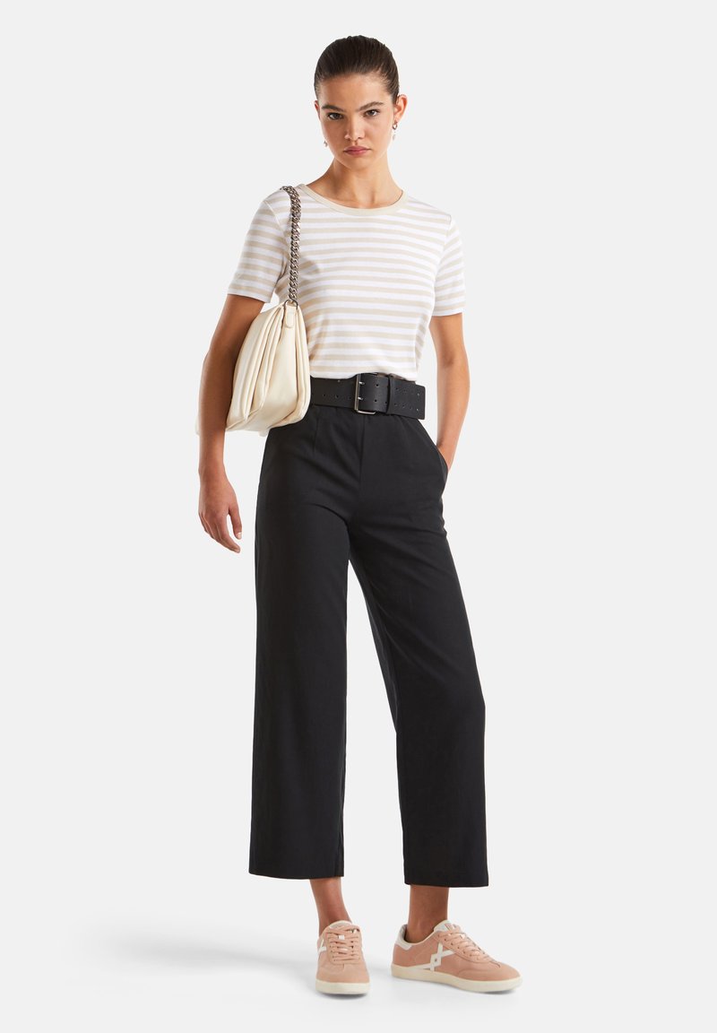 Gestreiftes Kurzarmhemd in Creme und Beige, hochtaillierte schwarze weit geschnittene Hose, übergroße cremefarbene Tasche und blassrosa Sneakers mit weißen Akzenten.