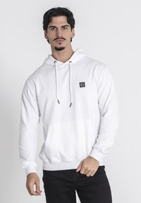 Biely mikina s kapucňou vyrobená z mäkkej tkaniny, s kloktanou kapsou, šnúrkami a malým čiernym logom na hrudi.