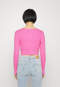 Rosa ribbat långärmad croppad tröja med rund halsringning och åtsittande ärmar, kombinerad med ljusblå högmidjade jeans.