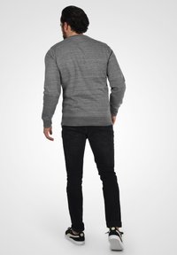 Maglione grigio lavorato a maglia con collo rotondo, motivo testurizzato, abbinato a jeans neri slim-fit e scarpe da ginnastica nere con suole bianche.