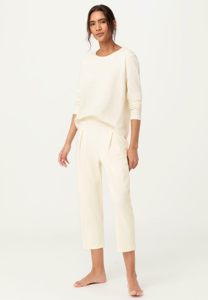 Cremfarbene, langärmlige, leichte Bluse kombiniert mit taillierten, cropped Hosen. Weicher Stoff mit subtiler Textur. Einfaches, entspanntes Design.