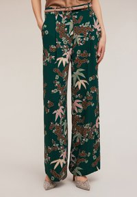 Breda byxor i mörkgrönt tyg med ett blommönster i rosa och bruna toner. Inkluderar framveck och sidofickor.