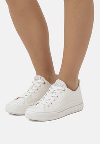 Weiße Canvas-Sneaker mit niedrigem Schnitt, runder Spitze, Schnürung vorne und Gummisohle. Mit einem dezenten Logo auf der Zunge und strukturierten Akzenten.