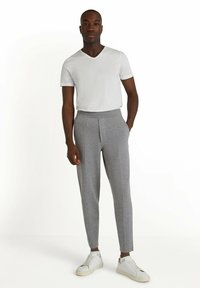 Grijze taps toelopende sweatpants met twee voorplooien, gecombineerd met een witte T-shirt met korte mouwen en V-hals, en witte sneakers. Soepele stoftextuur.