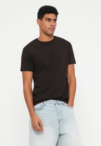 Svart kortärmad T-shirt i bomull, rund halsringning, slät textur; bärs med ljusblå denimjeans i avslappnad passform.