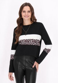 Schwarzes Langarmshirt mit weißen Streifen und einem Leopardenmuster-Band im unteren Bereich, kombiniert mit schwarzen Lederimitat-Hosen.