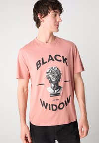 Krátký rukáv, světle růžové tričko s grafikou bystu a tučným textem "ČERNÁ VDOVA" v černé barvě, se zmíněným datem.