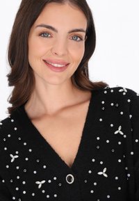 Czarny kardigan z dekoltem w serek, ozdobiony mieszanką fakturowanych koralików i kwiatowych akcentów, oraz dekoracyjnym zapięciem na guzik.