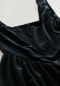 Schwarzes Samtkleid mit breiten Trägern und gerafftem Taillendetail, flach auf einem weißen Hintergrund ausgelegt.