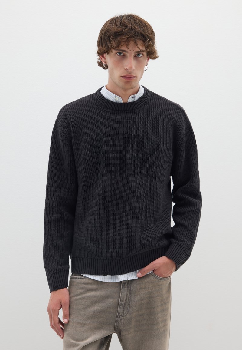 Schwarzer, gestrickter Pullover mit Rippstruktur und Rundhalsausschnitt, mit der Aufschrift "NICHT DEIN GESCHÄFT" in fettem, kontrastierendem Text.