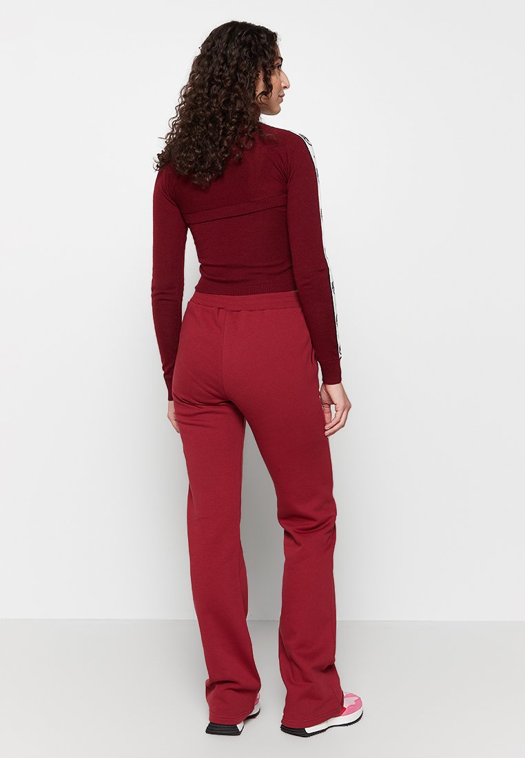 Bordeauxfarbener, figurbetonter Hoodie mit langen Ärmeln und gerippten Bündchen, kombiniert mit passenden, lässigen Jogginghosen. Glattes Material, minimalistische Details.
