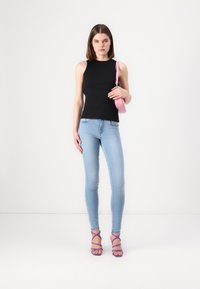 Top sin mangas negro con relieve, jeans ajustados azul claro y sandalias de tacón alto moradas con tiras; sosteniendo un pequeño bolso rosa.
