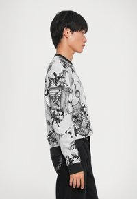 Μαύρη και λευκή ζακέτα με σχέδια, που διαθέτει λουλουδάτα και γεωμετρικά σχέδια, μακριά μανίκια και μαύρη ριμπ λαιμόκοψη και μανσέτες.